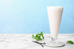 Scoop of Antler Farms vanilla whey protein beside a glass of shake.