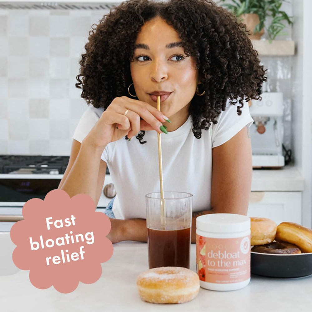 Spoonful of Debloat to the Max beside a glass of beverage.