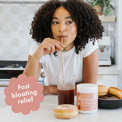 Spoonful of Debloat to the Max beside a glass of beverage.