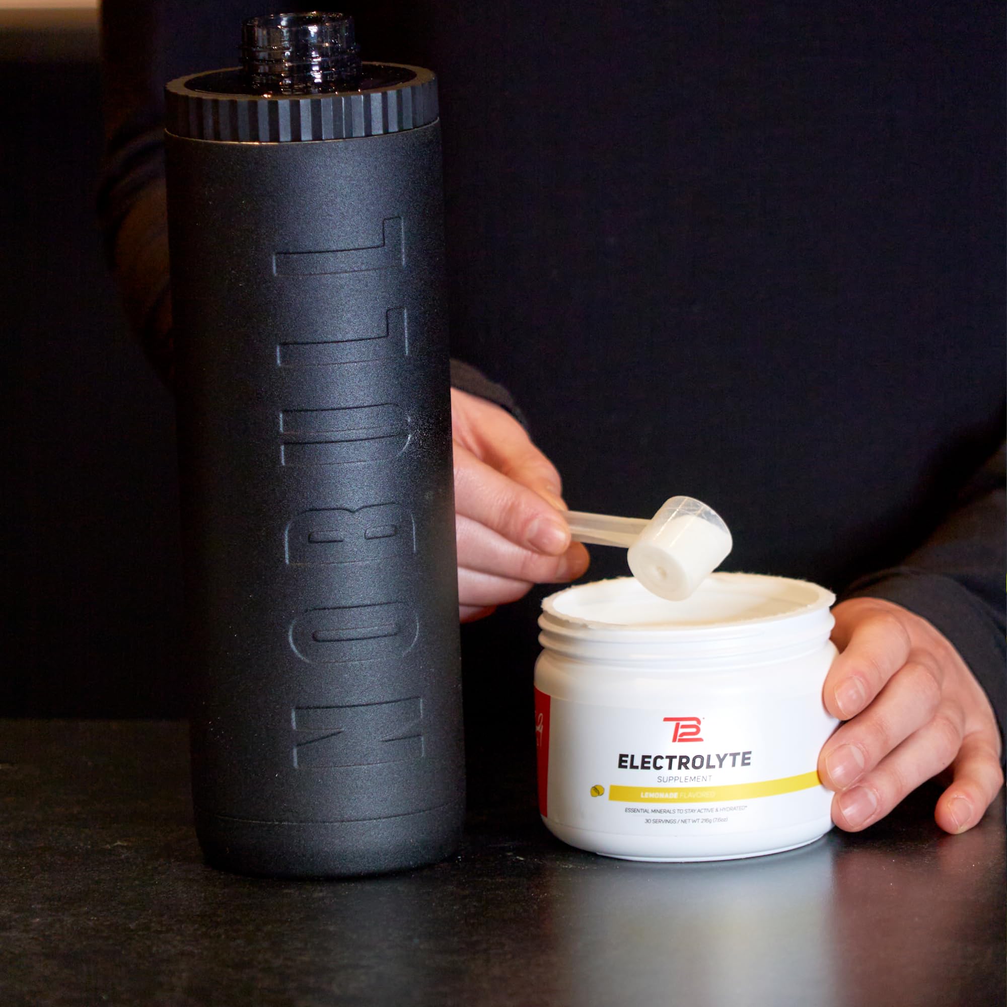 TB12 electrolyte powder near gym bottle for post-workout use.