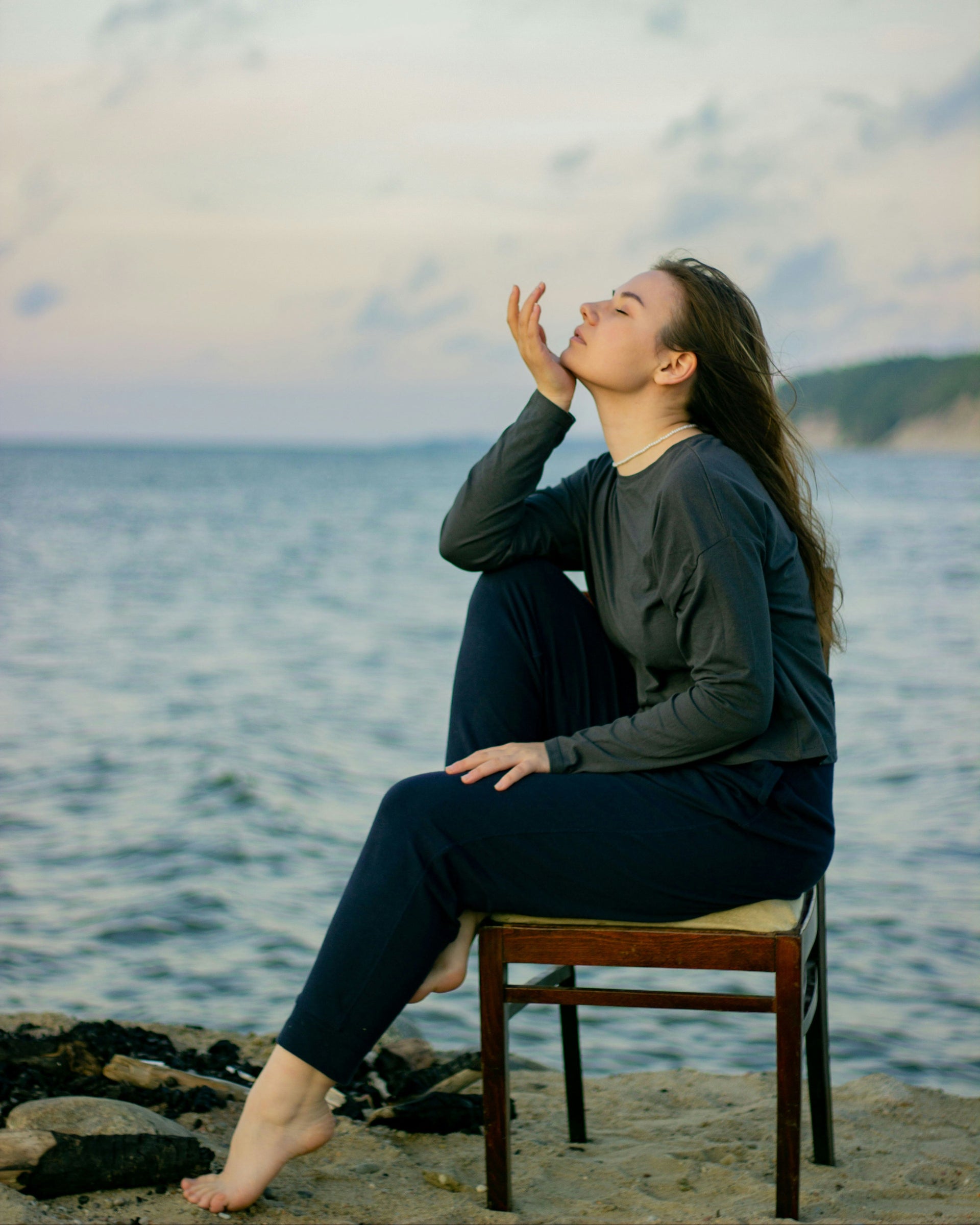 Woman sitting on a chair by the ocean with her hand shielding her eyes from the sun.